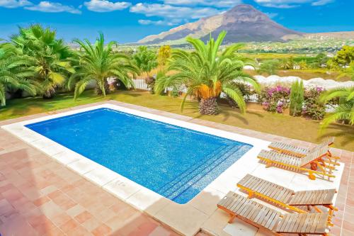 a swimming pool with palm trees and a mountain in the background at 0338 Villa Elefante Tia in Jávea
