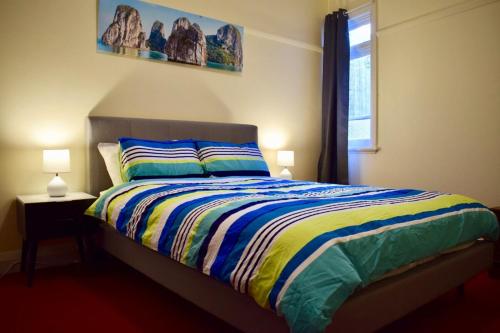 a bedroom with a bed with a colorful comforter and a window at Comfortable 3 Bedroom Apartment In Trendy Haberfield in Sydney