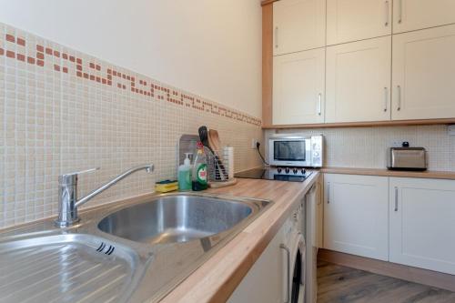 a kitchen with a stainless steel sink and white cabinets at Bright and Lovely 1 Bedroom Flat Belsize in London