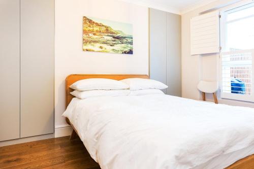 a white bedroom with a large bed with white sheets at Beautifully Styled Modern Apartment With Garden in London