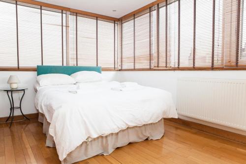 a bedroom with a bed with white sheets and windows at Spectacular Central 4-Bedroom Close To London Eye in London