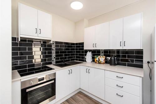 a kitchen with white cabinets and black tiles at Stylish Apartment in Leafy South Perth in Perth