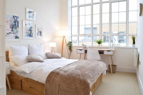 a bedroom with a large bed with a desk and windows at Bright Warehouse Conversion in Buzzing Peckham in London