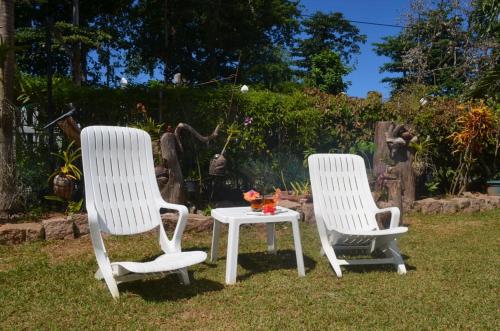 two white chairs and a table in the grass at Rising Sun Guesthouse in La Digue