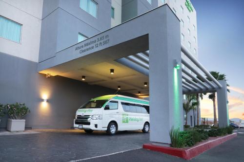 a white van parked in a parking lot next to a building at Holiday Inn Hotel & Suites Hermosillo Aeropuerto by IHG in Hermosillo