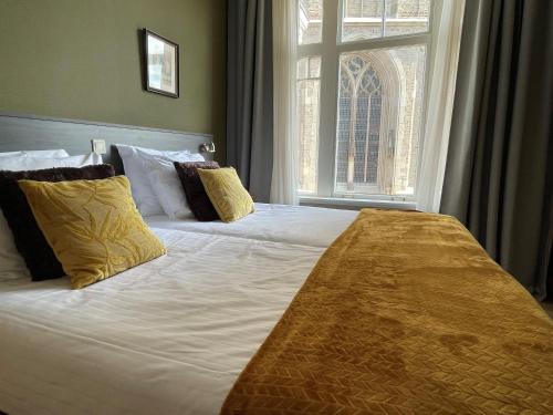a large bed with yellow pillows and a window at Hotel restaurant Stad Munster in Winterswijk