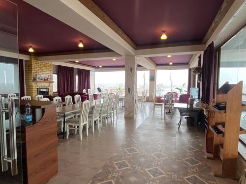 un restaurante con sillas blancas, mesas y ventanas en Uzumfermer Hotel & Winery, en Tashkent