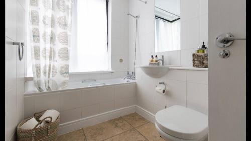 a white bathroom with a toilet and a tub and a window at 1 Farnsby Street Apartment 19 in Swindon