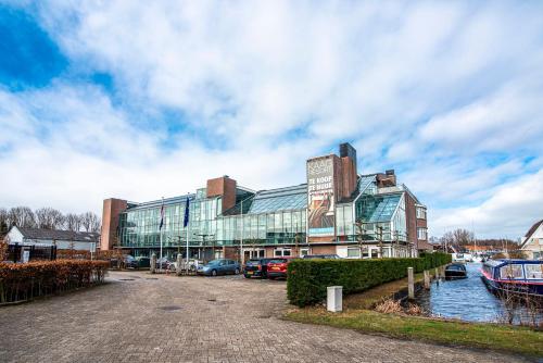 a large building with cars parked in front of a river at Kaag Resort in Warmond