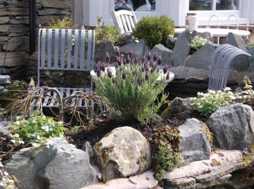 un jardín con rocas, flores moradas y sillas en White Rose, en Windermere