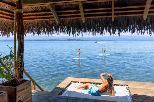 a woman laying on a pool in the water with two people on surfboards at Sol Bungalows Bocas del Toro in Bocas del Toro