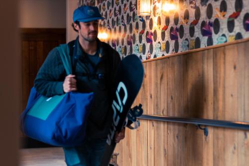 a man with a bag and a skateboard against a wall at The Bivvi Hostel Telluride in Telluride