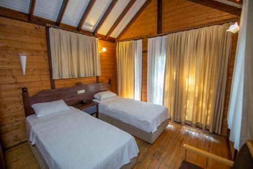two beds in a room with wooden walls and windows at Sea Valley Lodge in Faralya