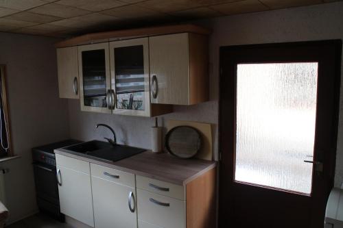 eine Küche mit weißen Schränken, einem Waschbecken und einem Fenster in der Unterkunft Ferienhaus Dani in Bad Gottleuba