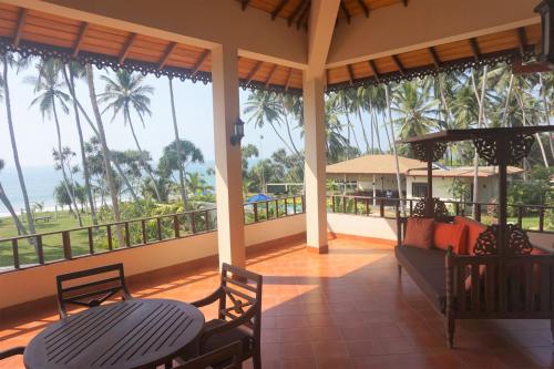 a porch with two tables and chairs and the ocean at Lanka Beach Boutique Bungalows & Grand Villa in Tangalle
