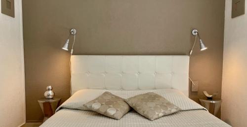 a bed with two pillows and two lights above it at Hotel L'Orangeraie in Le Lavandou
