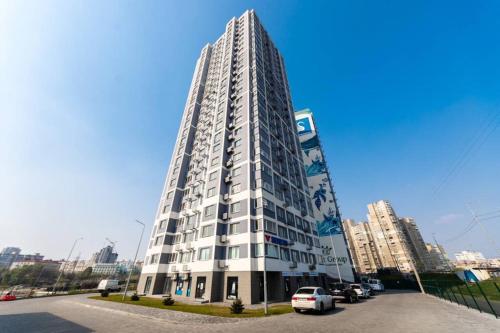 a tall white building with cars parked in a parking lot at Квартира люкс в ЖК Лебединый, ул. Ревуцкого 40 Г in Kyiv