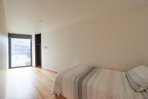 a white bedroom with a bed and a large window at Denison Rivulet Retreats in Bicheno