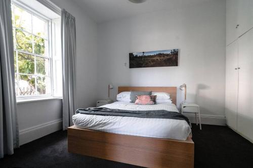 a bedroom with a bed with a wooden headboard and two windows at Berwick Cottage in Hobart