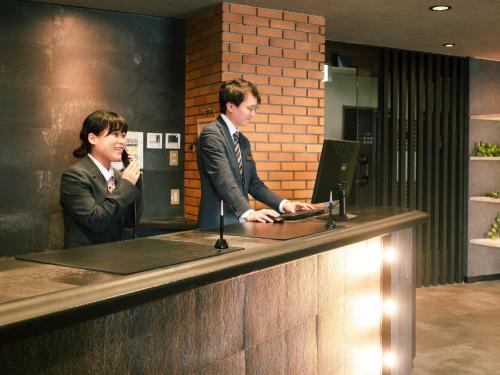a man and a woman standing at a reception counter at Hotel Area One Ise Inter in Ise