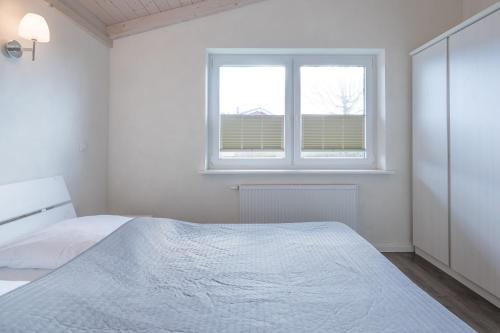a white bedroom with a bed and a window at Ferienhaus Pellworm in Dagebüll