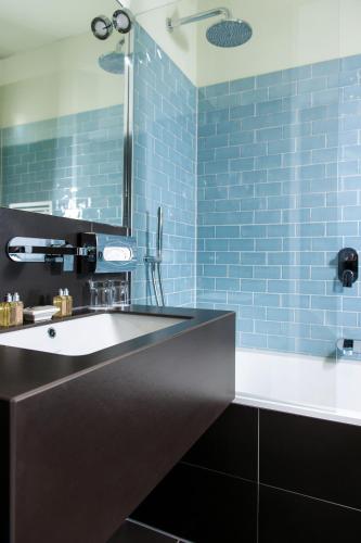 a bathroom with a tub and a sink and blue tiles at Clipper Boardinghouse - Berlin-Gendarmenmarkt in Berlin