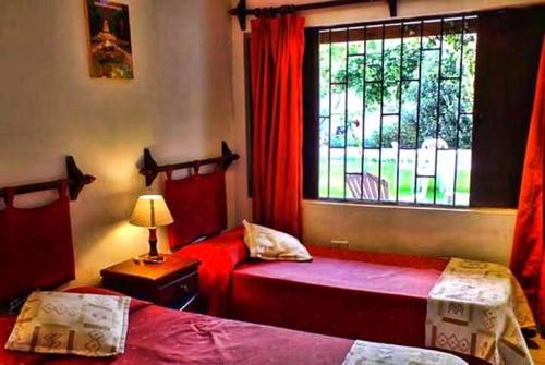 1 dormitorio con 2 camas y una ventana con cortinas rojas en Hotel inty raimi en Salta