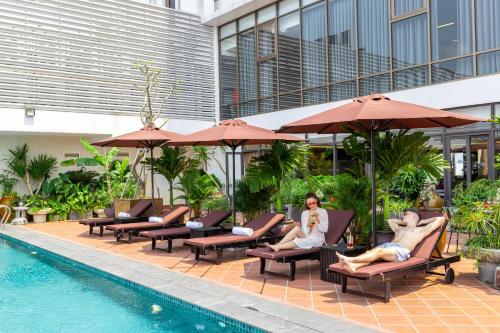 two people sitting in lounge chairs next to a swimming pool at White Lotus Hue Hotel in Hue