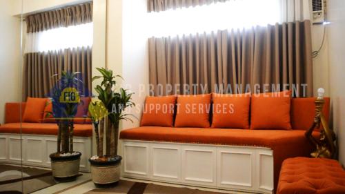 an orange couch in a room with curtains and plants at East Bay Residences @ Sucat Muntinglupa in Manila