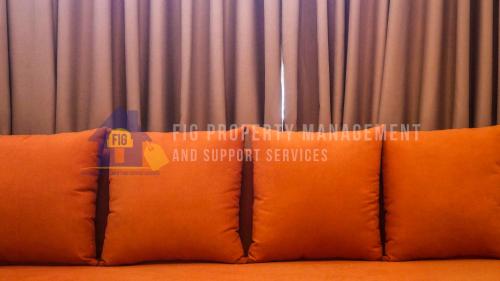 a couch with two orange pillows in front of a curtain at East Bay Residences @ Sucat Muntinglupa in Manila