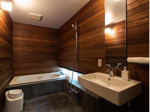 baño con paredes de madera, lavabo y bañera en Sekka Ni Chalet, en Niseko