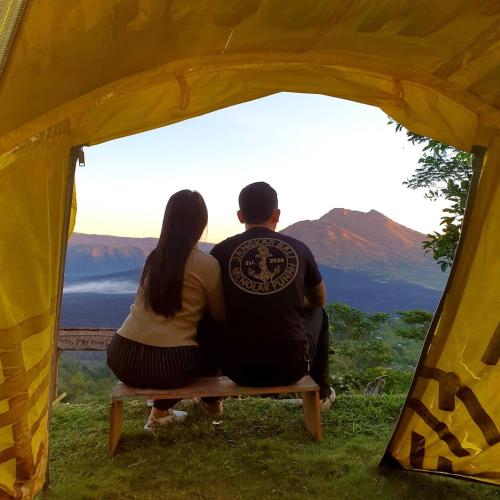 a man and woman sitting on a bench in a tent at Tukadsari camping in Kintamani