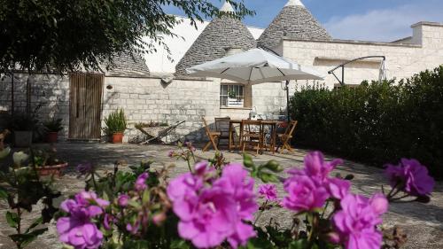 a house with a table and an umbrella and purple flowers at Trulli di Rosa in Locorotondo