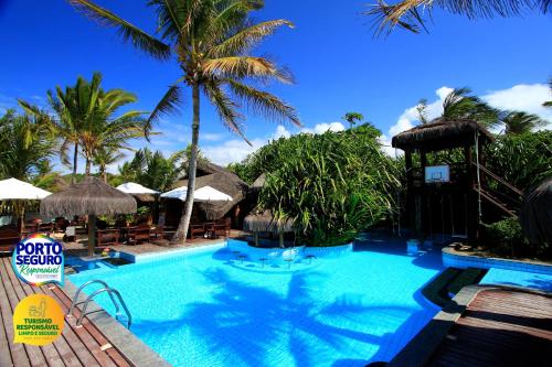 uma piscina com palmeiras e guarda-sóis em Beijamar Praia Hotel em Arraial d'Ajuda