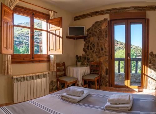a bedroom with a bed and a table and windows at Hotel Rural Fuente La Teja in Güéjar-Sierra