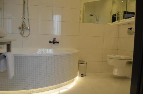 a white bathroom with a tub and a toilet at Hotel Alexandra in Pobiedziska