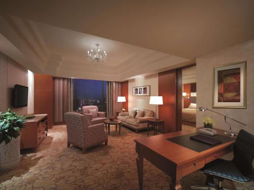 a hotel room with a desk and a living room at Shangri-La Huhhot in Hohhot