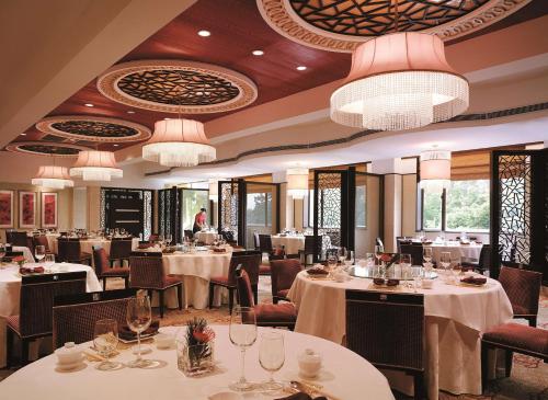 un ristorante con tavoli e sedie bianchi e lampadari a braccio di Shangri-La Hangzhou a Hangzhou