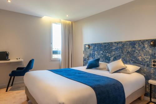 a hotel room with a large bed with a blue blanket at The Originals Boutique, Hôtel Porte de Dieppe in Saint-Aubin-sur-Scie