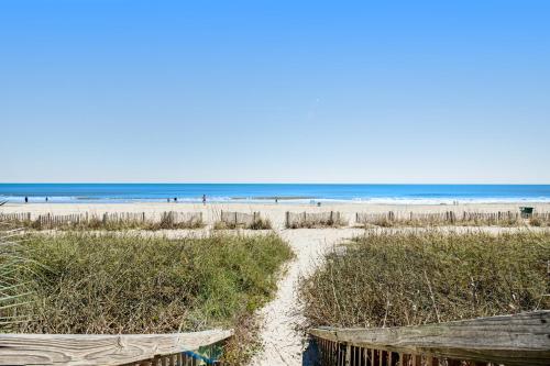 a beach with sand and grass and the ocean at Ocean Park Resort - Oceana Resorts Vacation Rentals - by Vacasa in Myrtle Beach