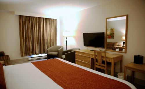a hotel room with a bed and a desk and a television at Auberge du Grand Lac in Magog-Orford