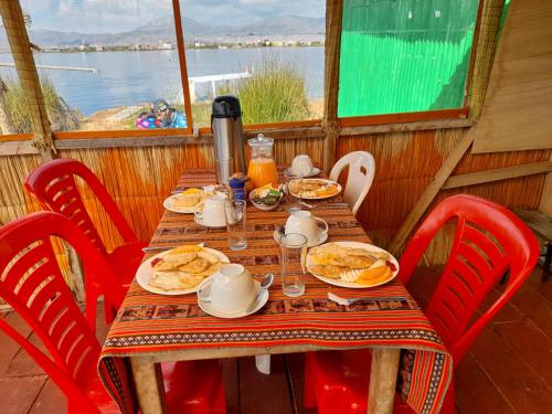 a table with plates of food on it with red chairs at Uros Lodge Lover Titiqaqa in Puno