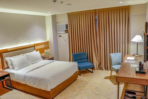 a bedroom with a bed and a desk and a blue chair at Acacia Hotel Bacolod in Bacolod