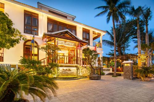 a building with palm trees in front of it at Hoi An Riverside Villas & Apartments in Hoi An