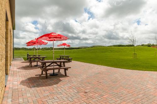 two picnic tables with red umbrellas in a field at Holiday Inn Express - Bodmin - Victoria Junction by IHG in Bodmin