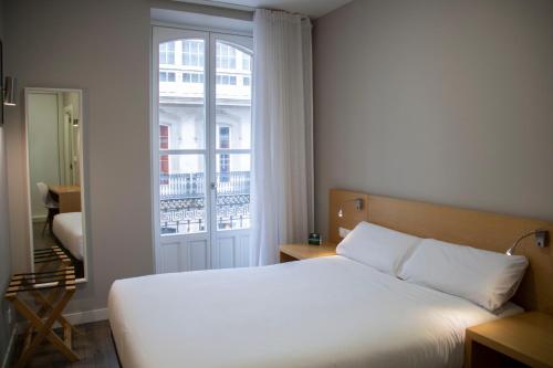 1 dormitorio con cama blanca y ventana en Alda Alborán Rooms, en A Coruña