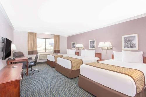 a hotel room with three beds and a desk at Days Inn by Wyndham Indio in Indio