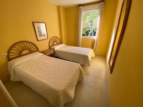 Cette chambre comprend 2 lits et une fenêtre. dans l'établissement Apartamentos Jardines del Puerto Altamar, à Alcossebre