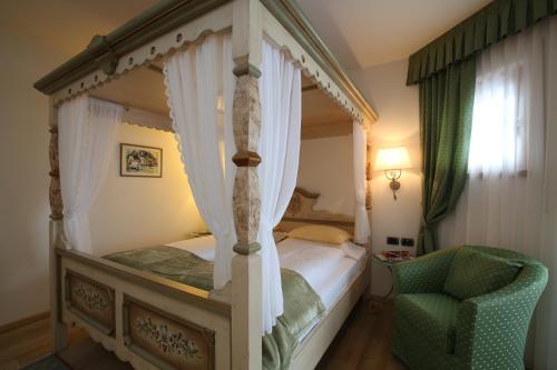 a bedroom with a four poster bed and a chair at Hotel Mesdi in Arabba