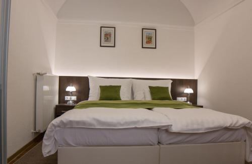 a white bedroom with a large bed with green pillows at Mecset Apartman in Eger